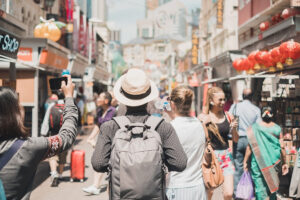 Vista trasera de un grupo de turistas caminando por una concurrida calle peatonal decorada con farolillos rojos chinos.